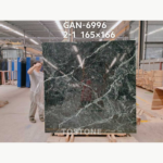 Greek Verde Alpi marble slab on timber supports, with intersecting pale veins and a worker standing beside it.
