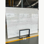 Angled view of a Guangxi White Marble slab with gently flowing gray veining, marked D