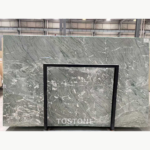 Iranian Green Marble slab behind a black display frame, showing pale green-grey tones and white veining