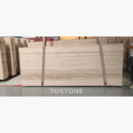 Front view of a Pakistan travertine slab with cream and beige horizontal bands, secured by two lifting straps.