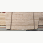 Pakistan travertine slab on timber supports, showing pale beige layers and a broad warm band across the centre.