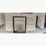Pakistan travertine slab behind a black display frame, with wavy cream and grey-beige horizontal bands.