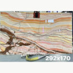 Rainbow Agate Marble slab with cream, amber and pink horizontal bands and bold brown branching patterns at the lower left.