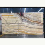 Rainbow Agate Marble slab with narrow cream and gold bands crossed by grey diagonal lines, held by a lifting clamp.