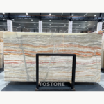 Rainbow Agate Marble slab with fine horizontal grey, cream and rust bands behind a black display frame.