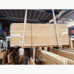Rosin Jade Marble slab in a warehouse, showing a golden field, fine cream layers and a curved pattern on the right.