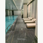 Indoor pool reference image showing dark grey stone flooring beside turquoise water and pale lounge chairs.