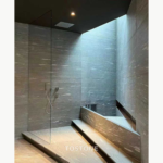 Shower interior reference image with fine-streaked grey stone surfaces, a glass screen and a stepped bathing area.