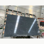 Sandalwood Snow Marble slab on workshop equipment, showing a dark charcoal field with fine pale streaks.