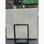 Snow White Marble slab with a milky white surface and faint warm accents, displayed behind a black support frame.
