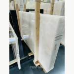 Angled detail of stacked Snow White Marble slabs with ivory tones, a fine honey-coloured line and visible slab edges.