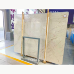 Oblique view of Sofitel Gold Marble with slender brown veins over a warm cream base and wooden packing supports.
