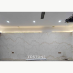 Interior wall reference using Straight Vein White Jade Marble panels with broad grey-beige wave patterns beneath ceiling lighting.