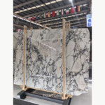 Turkish Calacatta Viola Marble slabs held in a wooden rack, showing broad pale areas and branching dark veins.