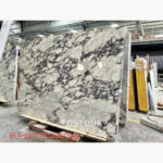 Turkish Calacatta Viola Marble slab with broad ivory areas and diagonal dark veining in a warehouse.