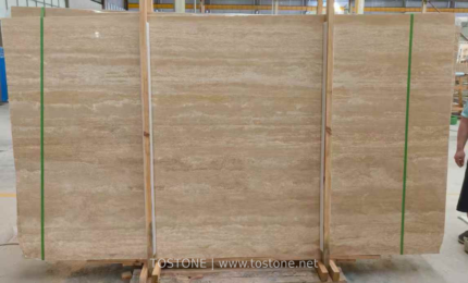 Turkish cream travertine slabs secured with wooden supports and green straps, showing beige horizontal layers