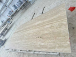 Angled view of a Turkish cream travertine slab lying flat in a workshop with flowing beige and ivory bands
