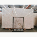 White Crystal Marble slab on a warehouse rack, showing a glossy white surface with fine intersecting lines and warm brown veins.