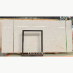Wide White Mushroom Marble slab with a soft ivory base and irregular gray-beige details behind a black support frame.