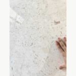 Close-up of White Mushroom Marble showing fine gray flecks and larger beige markings beside a hand.