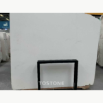 White Sand Beige Marble slab showing a softly mottled off-white surface behind a black display stand.